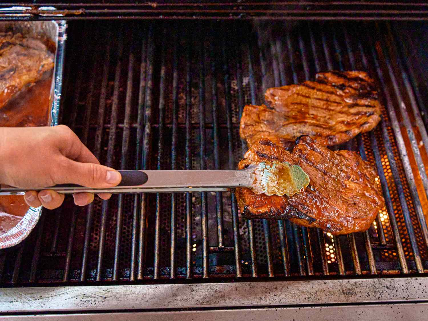 Person grilling pork steaks with tongs on a grill