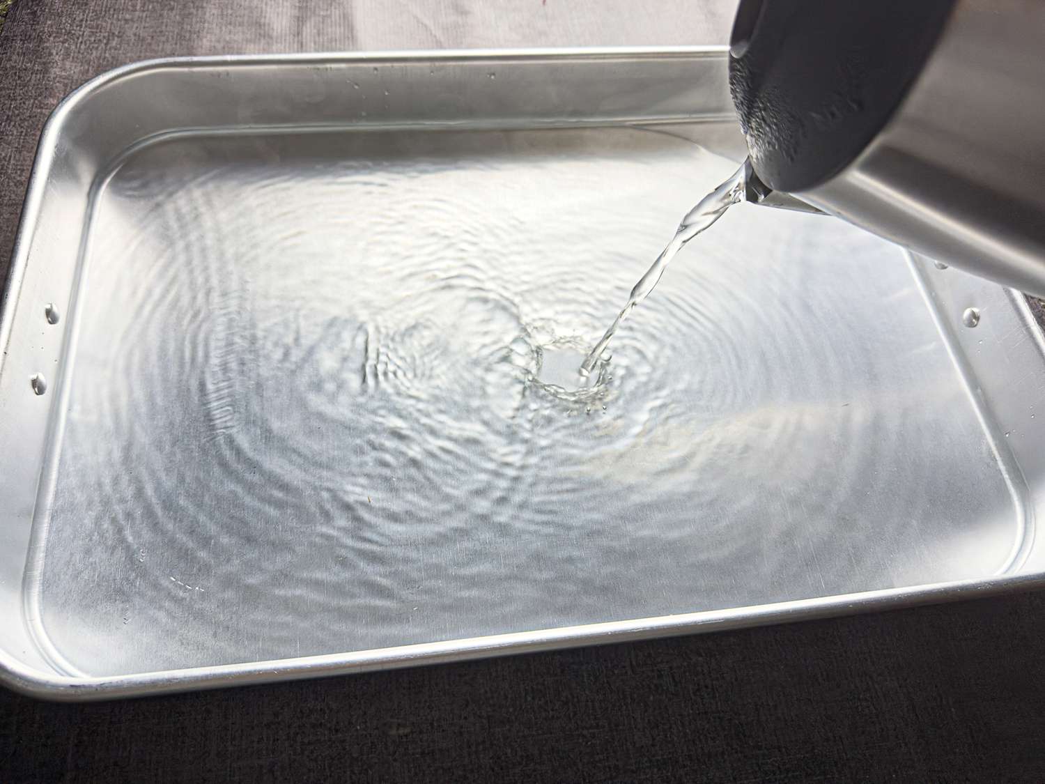 Water being poured into a baking pan from a kettle, preparation step for a recipe