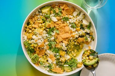 A bowl of corn salad with various toppings, photographed with vibrant background colors