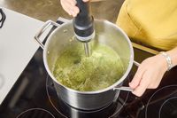 A person uses the KitchenAid Go Cordless Hand Blender to make soup