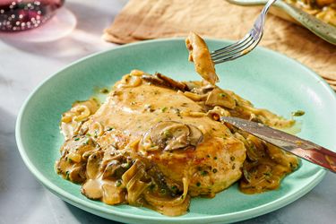 A plate with chicken fricassee served with mushroom sauce a fork lifting a piece of chicken