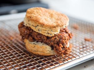 A kimchi fried chicken black sesame biscuit sandwich on a wire rack set over a rimmed baking sheet