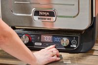 A person pressing a button on the Ninja Woodfire 8-in-1 Outdoor Oven