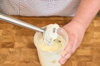 A person uses the All-Clad Stainless Steel Immersion Blender inside a plastic container