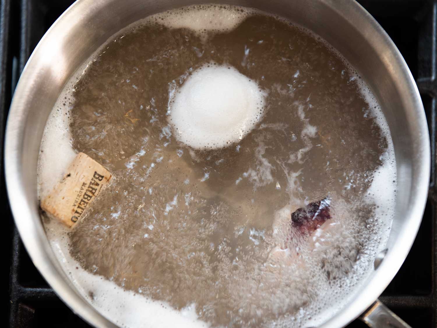 Looking down into a boiling pot on the stovetop, with a piece of octopus and a cork in the water.