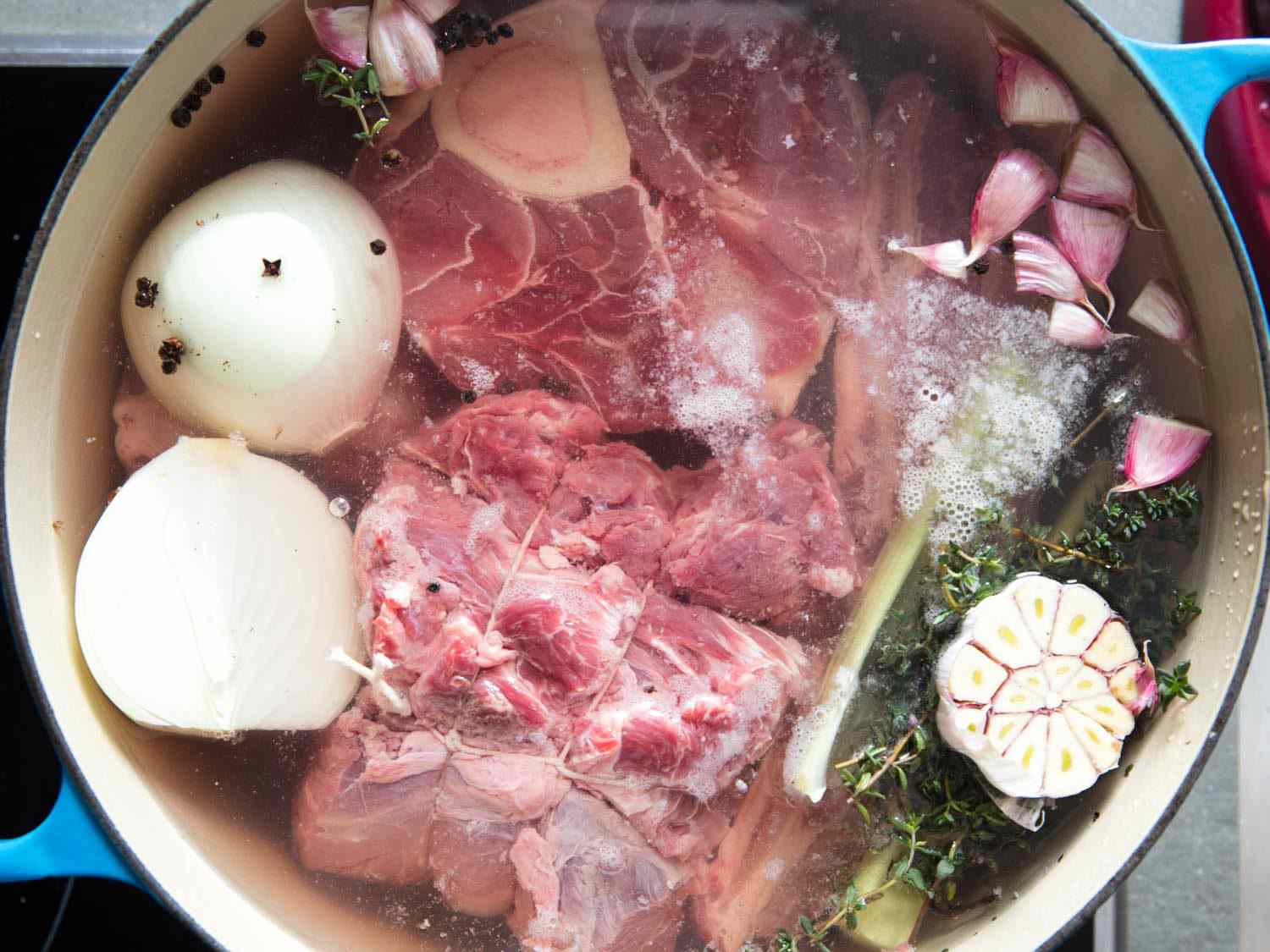 Cuts of beef in a Dutch oven with an onion and head of garlic.