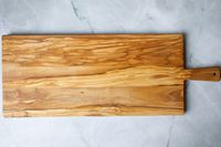 A wooden charcuterie board with a handle on a marble countertop.