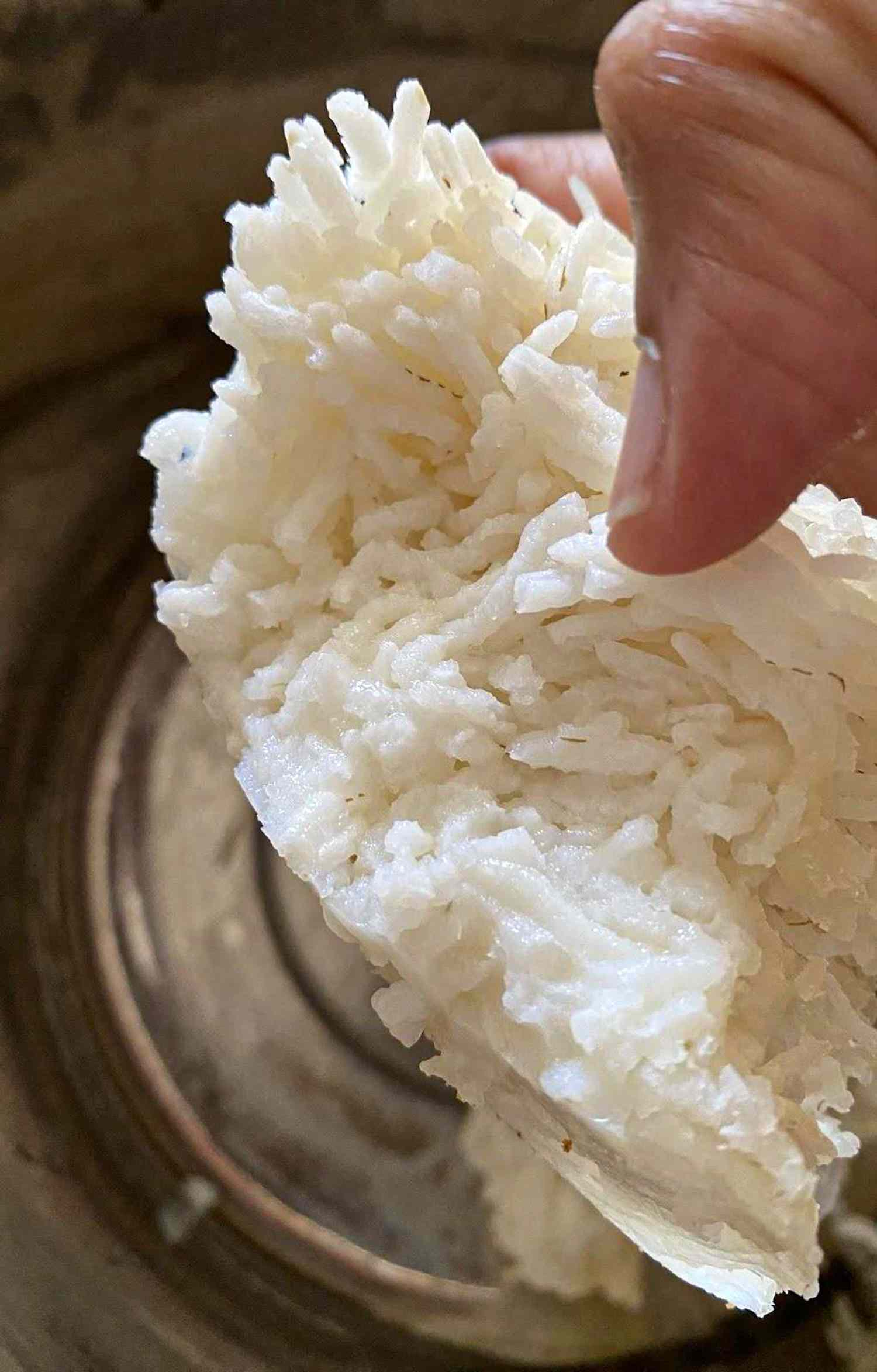 A person holding a portion of rice near a metal pot