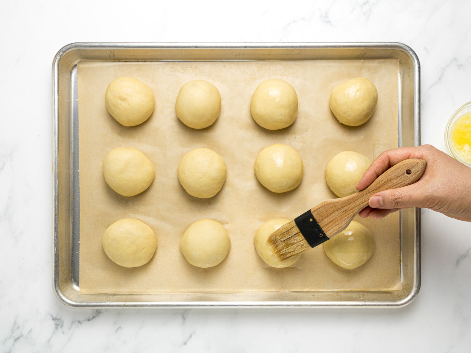 Brushing dough balls on a sheetpan with butter 