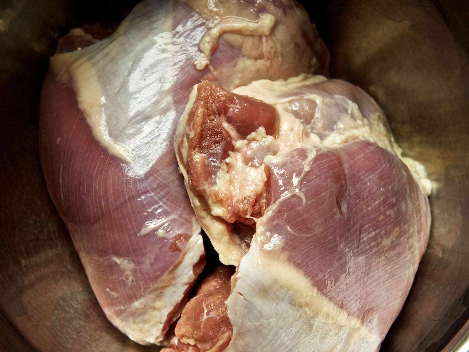 Closeup of a pair of raw, boneless turkey thighs in a mixing bowl.