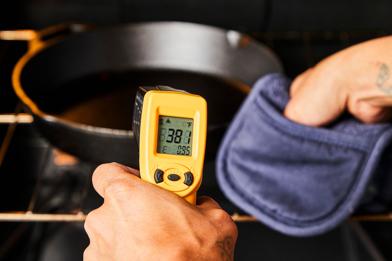 a person grabbing a cast iron skillet with a pot holder and taking the temperature with an infrared thermometer