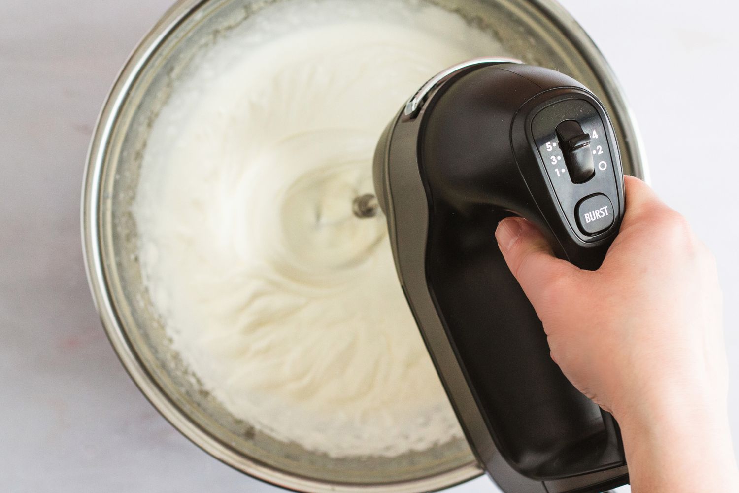 A person using a hand mixer to make whipped cream.