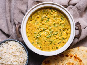A double-handled serving crock with chickpea, coconut, and cashew curry. Some naan and a bowl of steamed rice are next to it. 