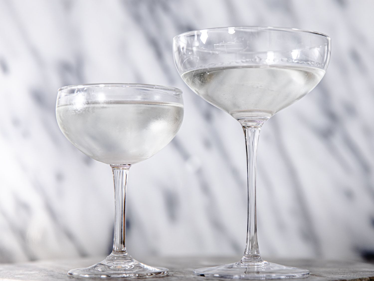 one small and one large coupe glass side by side, both with the same amount of liquid in them