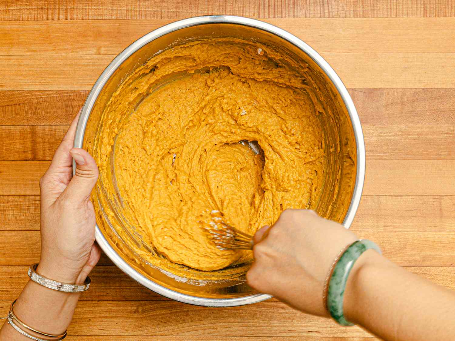 Hands mixing pumpkin pancake batter in a bowl with a whisk