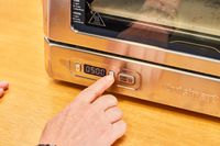 A person presses a button on the Cuisinart CPZ-120 Stainless Steel Indoor Pizza Oven