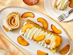 Plated dessert with rolled crepes sliced peaches and cream topping