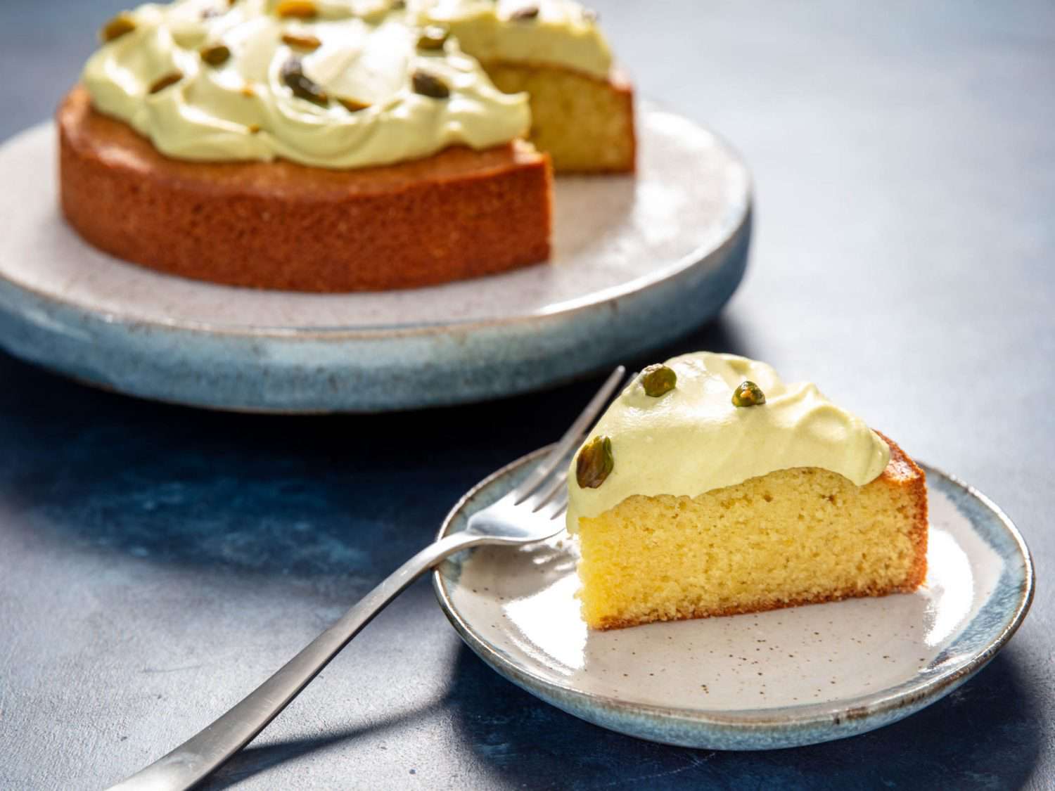 Pistachio oil cake with a slice cut out onto a serving plate. 