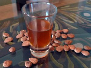 A flared shot glass of DIY amaretto, surrounded by whole raw almonds.