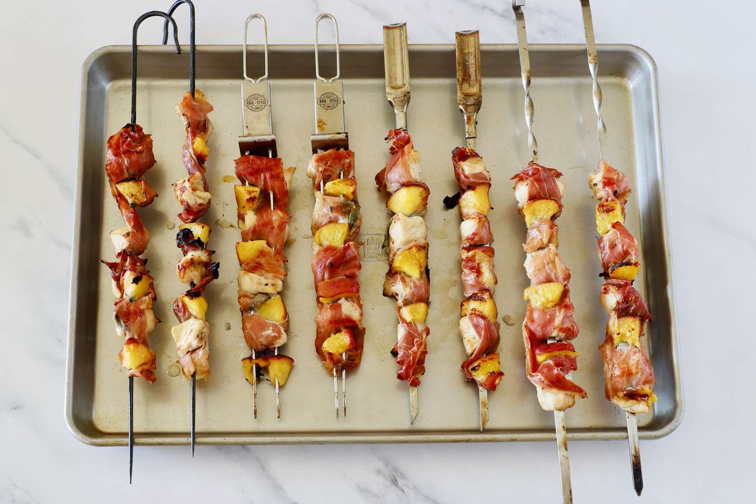 8 skewers loaded with chicken, peach, and prosciutto on a metal sheet tray