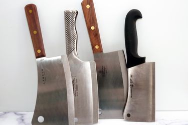 four meat cleavers standing on a marble surface with a white backdrop