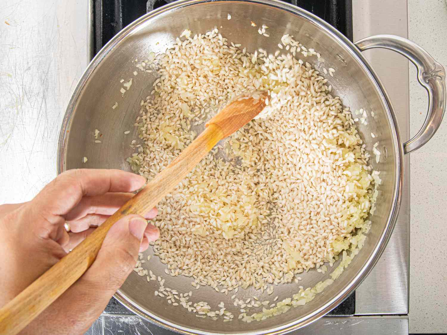 Overhead view of adding rice to onions and toasting