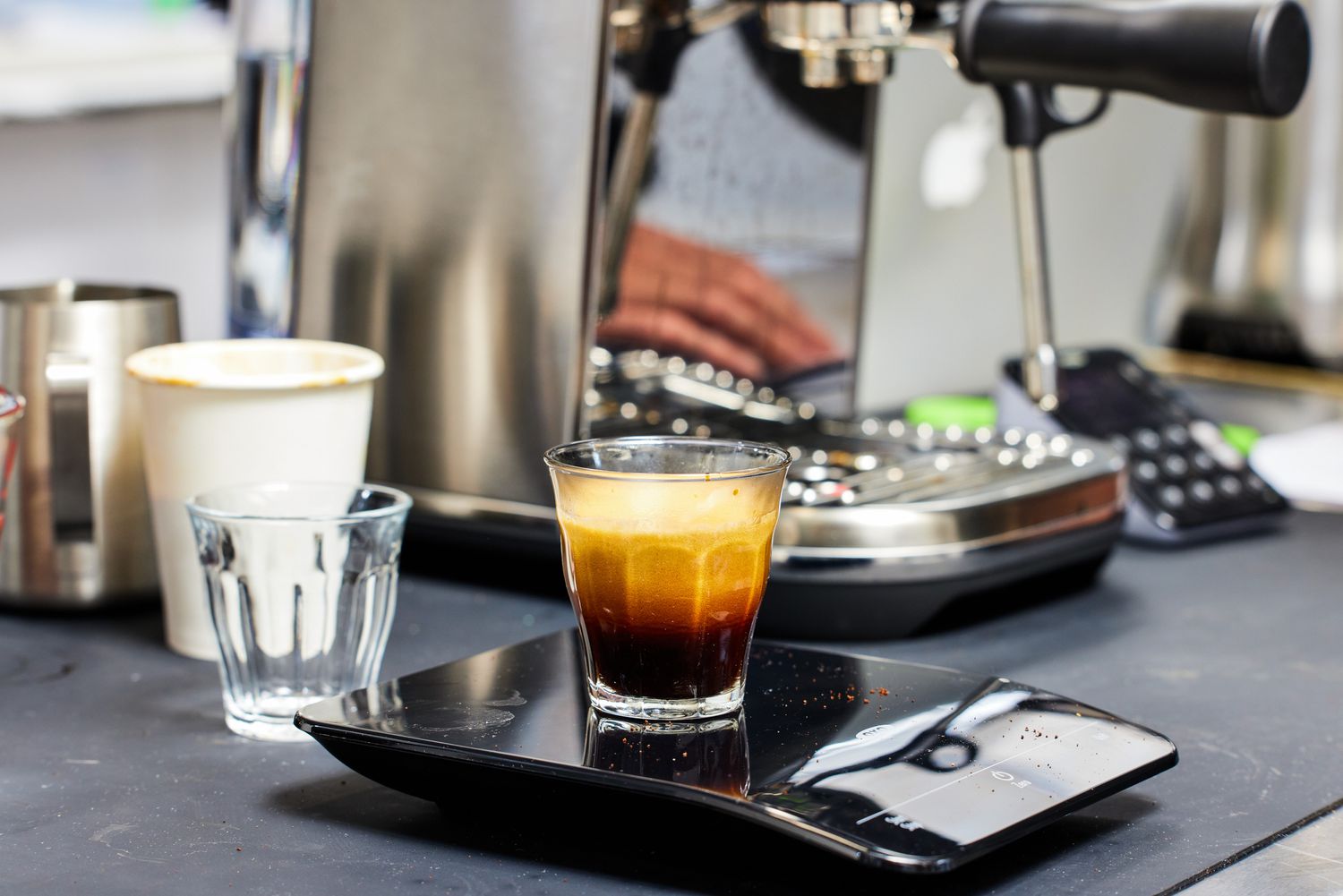 Espresso coffee in a clear cup on kitchen scale next to Breville Bambino Plus Espresso Machine