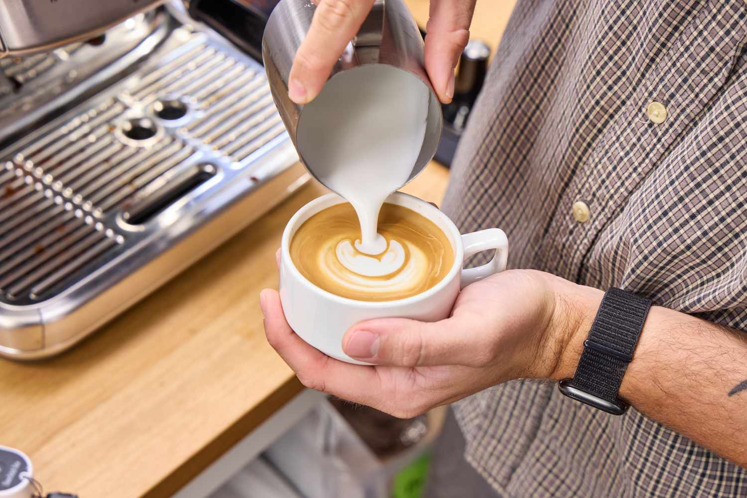 A person pours steamed milk into an espresso made in the Breville The Barista Pro Espresso Machine