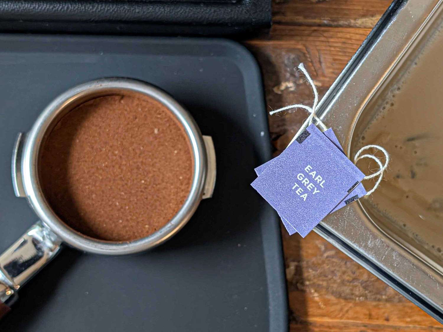 Portafilter filled with ground coffee and tea bag tags labeled 'Earl Grey Tea' next to brewing equipment