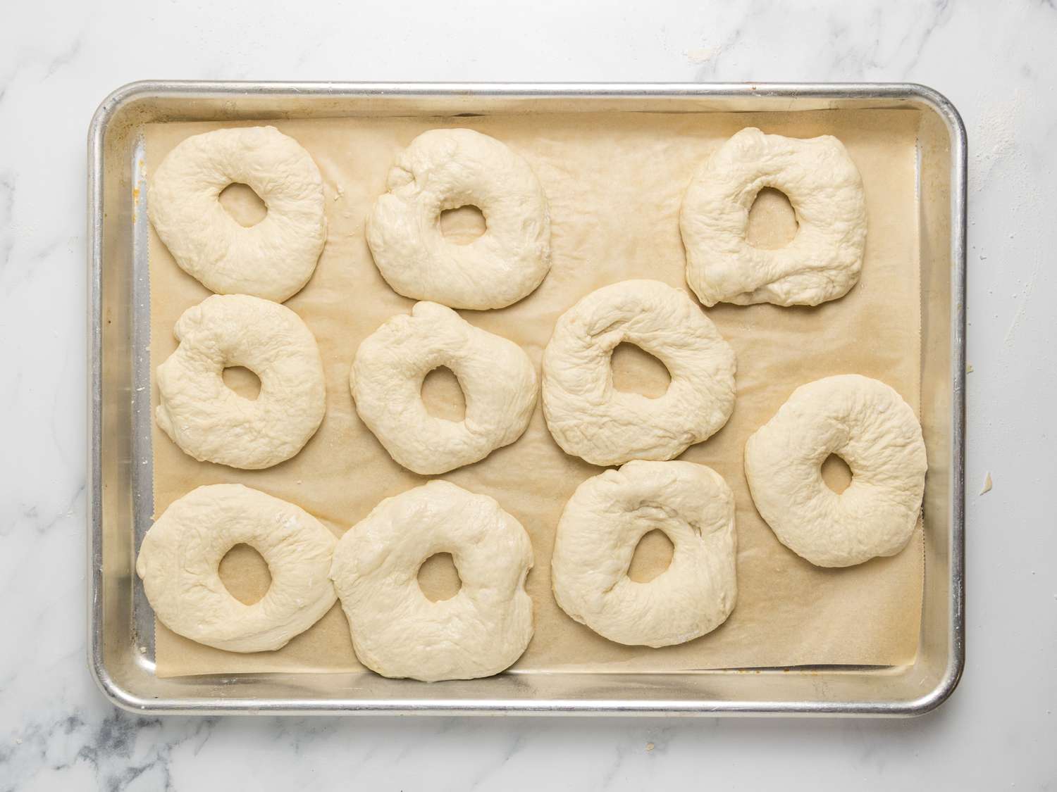 Ten pieces of dough with holes in the center on a parchment-lined baking sheet