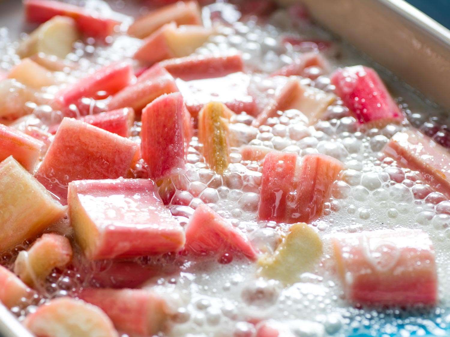 Chopped rhubarb in a baking dish, surrounded by a foaming liquid