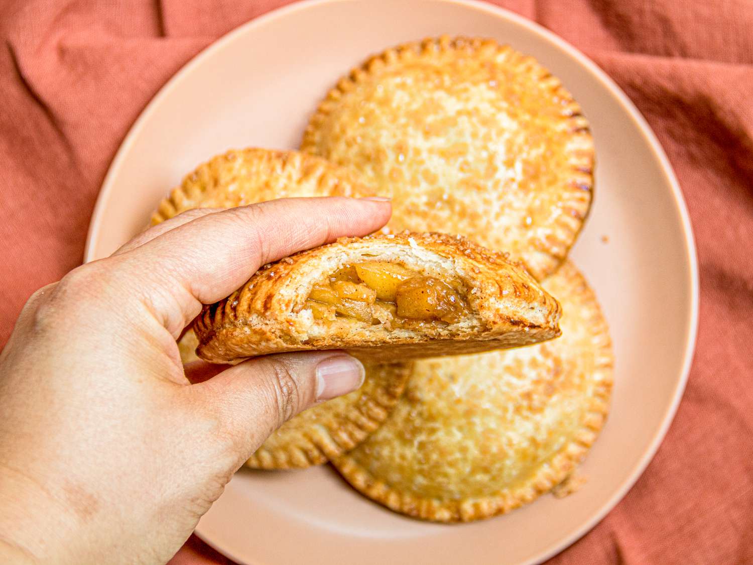 Overhead view of a hand holding an apple hand pie with a bite taken out of it 