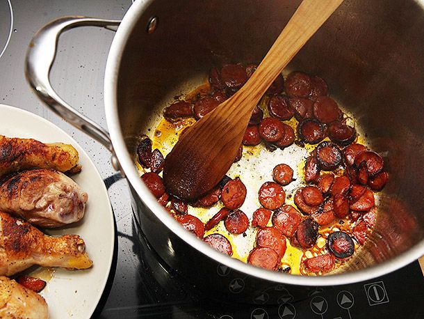 Browning sliced chorizo in a stock pot of oil and rendered chicken fat. Browned chicken is on a white plate in the background.