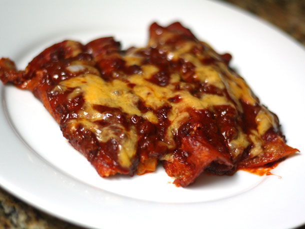 A plate of 3 Tex-Mex enchiladas covered with red chile gravy and melted cheese.