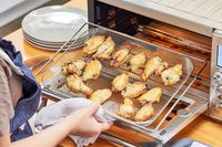 A hand removing cooked chicken wings from the Breville the Smart Oven Air Fryer