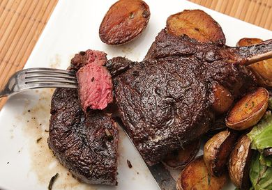 A forkful of medium rare meat cut from a butter-basted bison rib steak plated with crispy potatoes