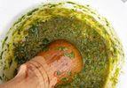 A mortar and pestle filled with a green herb-based sauce (pistou)