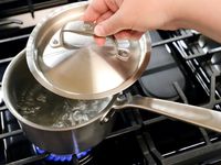 Person lifting lid from Made In Stainless Clad Saucepan with boiling water