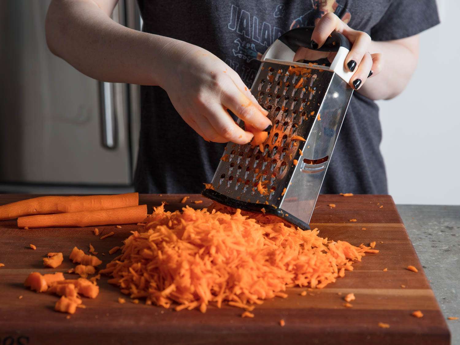 Grating carrots on the holes of a box grater, on a wooden cutting board.