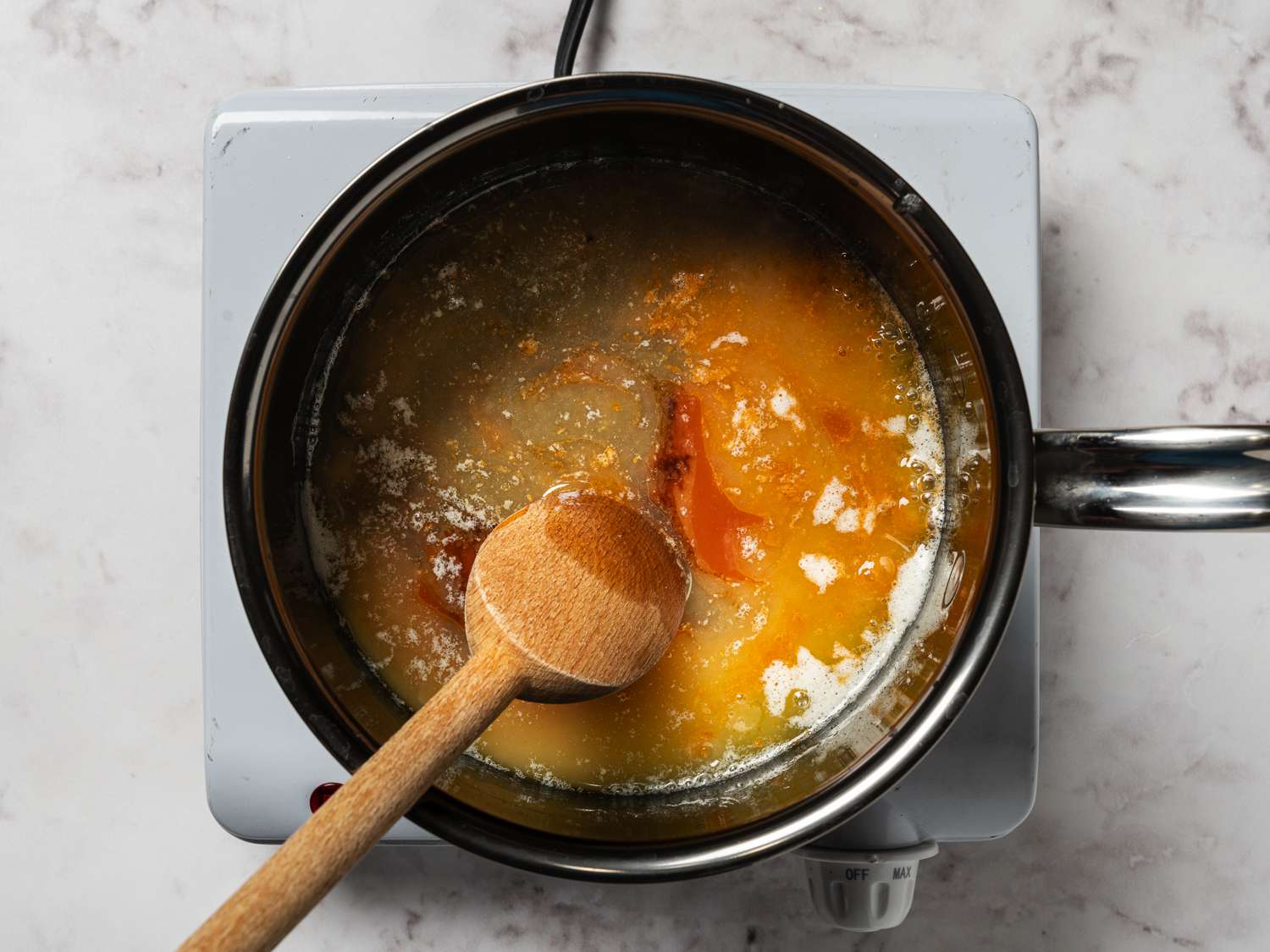 A stainless steel saucepan holding the sauce ingredients which are being stirred together with a wooden spoon.