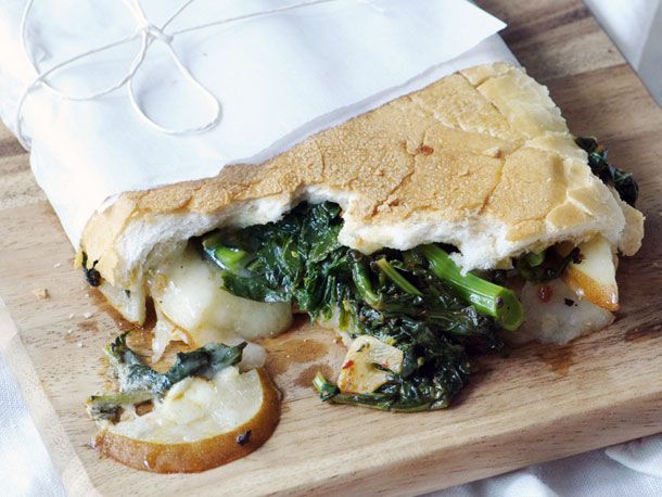 Closeup of a half-eaten Broccoli Rabe, Pear, and Fontina Sandwich. The sandwich has been wrapped in a wax paper "diaper."