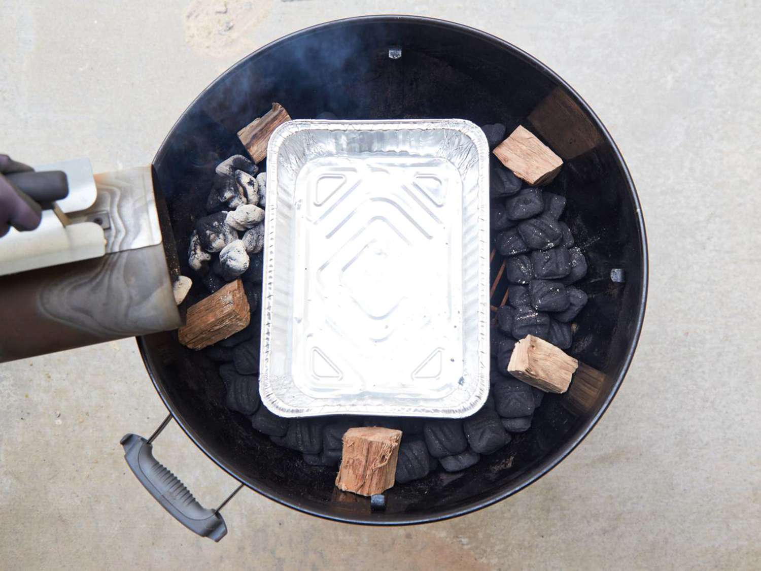 A BBQ smoker setup with wood chunks, charcoal, and a water pan in place for indirect smoking