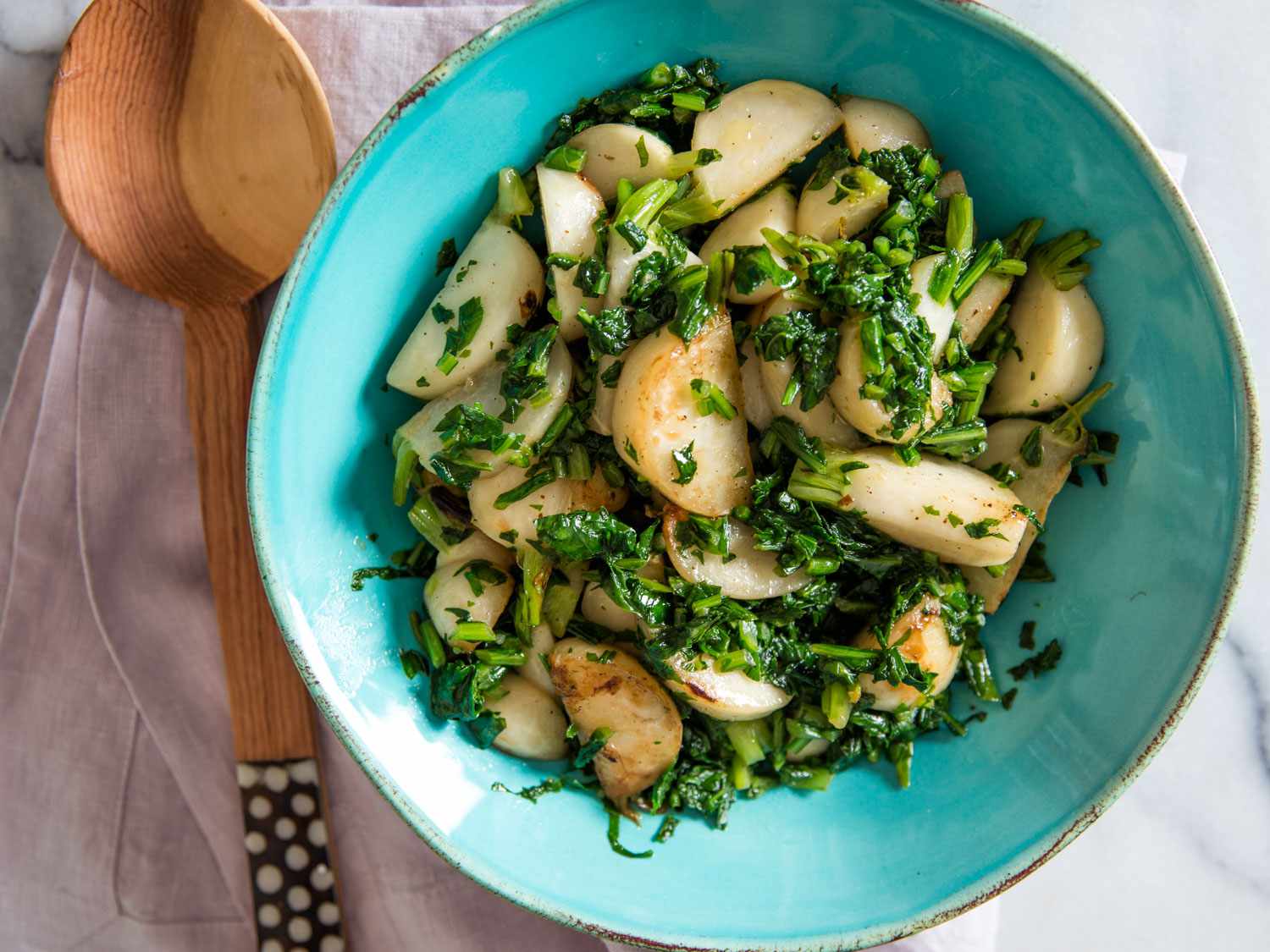 Overhead shot of sautéed Hakurei (Japanese) turnips and greens in a turquoise serving bowl.