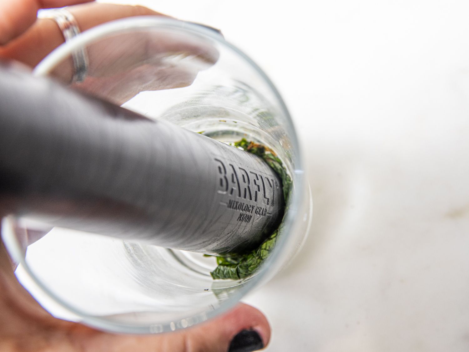 An overhead look at a muddler muddling mint leaves in a glass