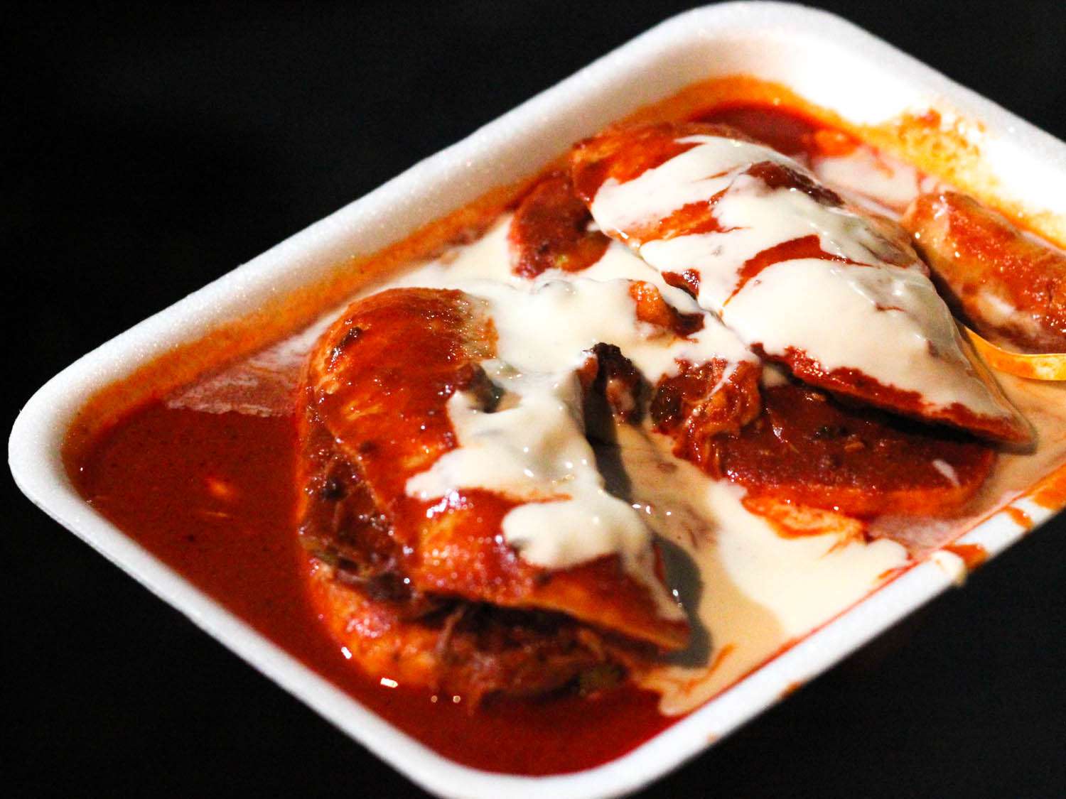 two small chanclas sandwiches drenched in red chile sauce and crema