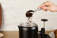 A person adding coffee grounds to the Fellow gooseneck kettle.