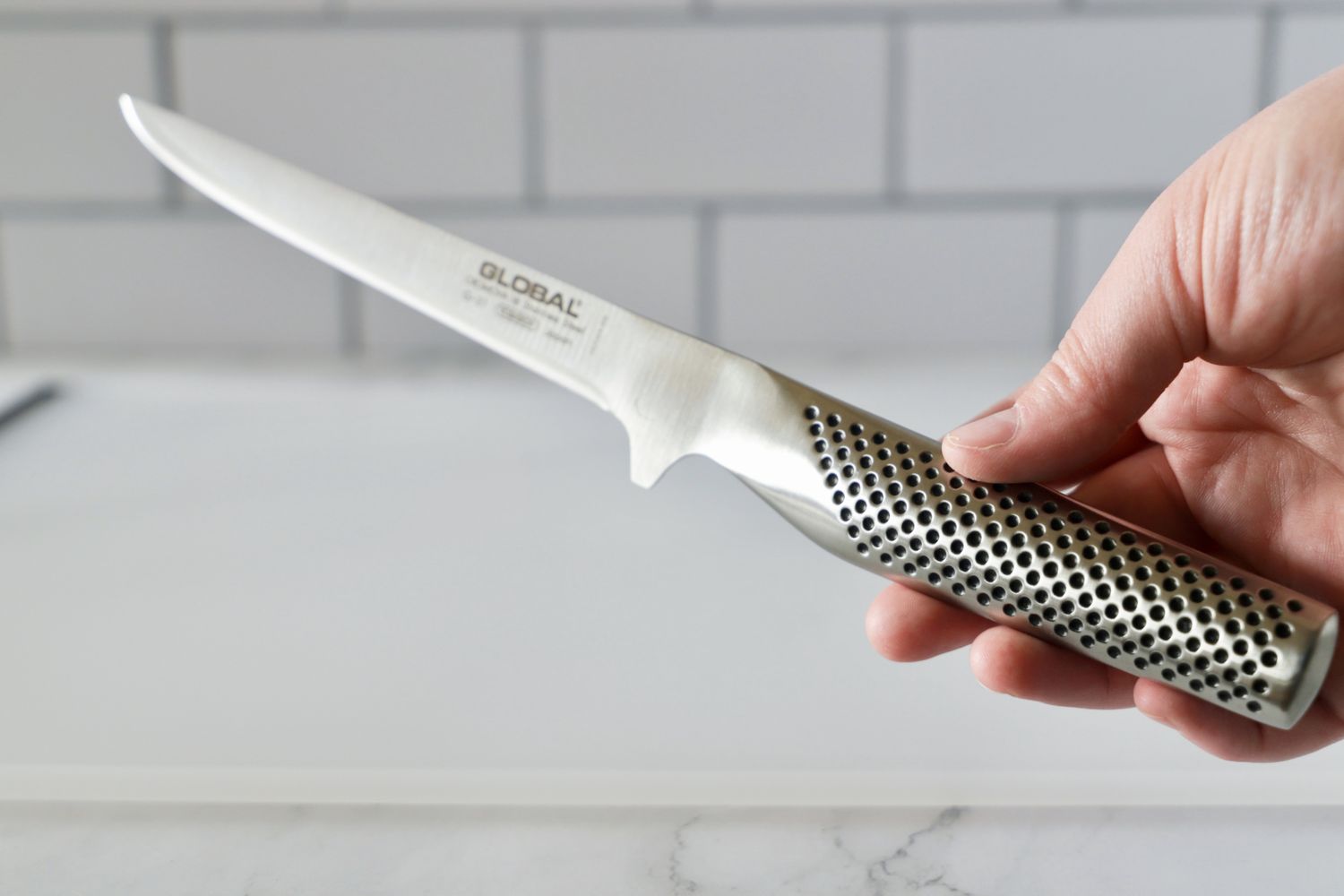 A person holding the handle of the Global boning knife.