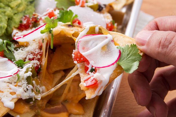 Closeup of a chip being pulled from a pan of fully-loaded nachos.