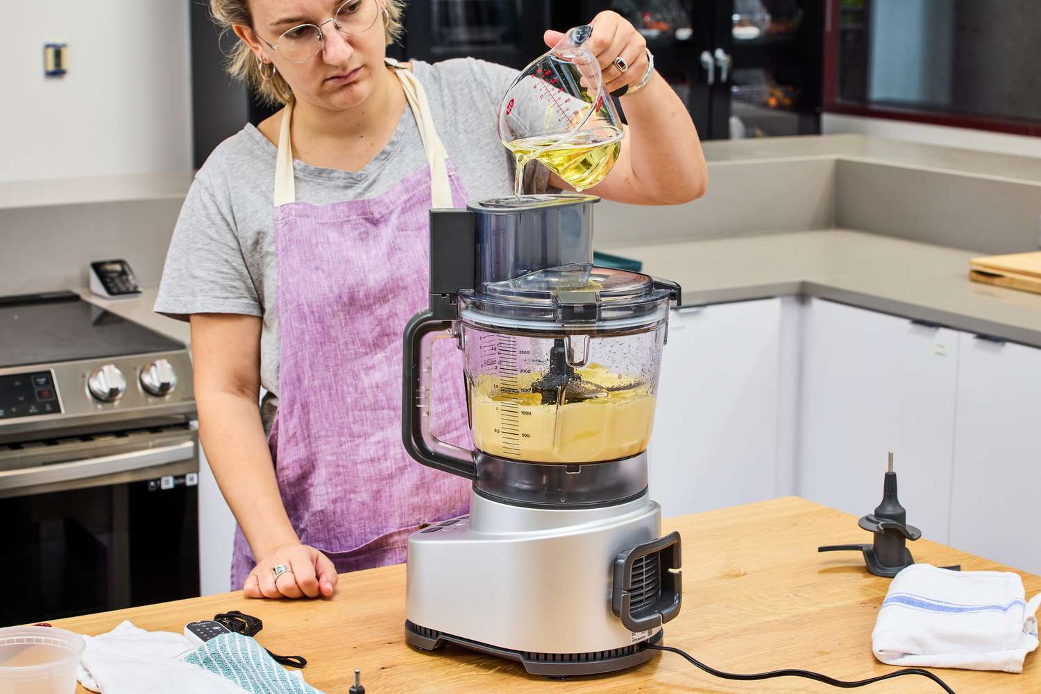 A person adding oil from a measuring cup into a food processor. 