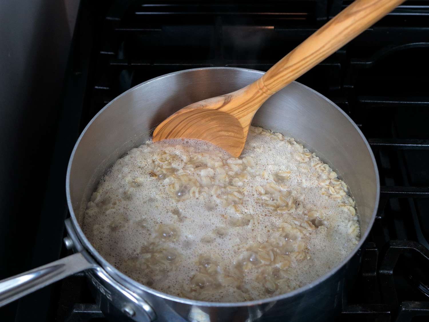 a spoon with a rounded bowl stirs oatmeal in a pot